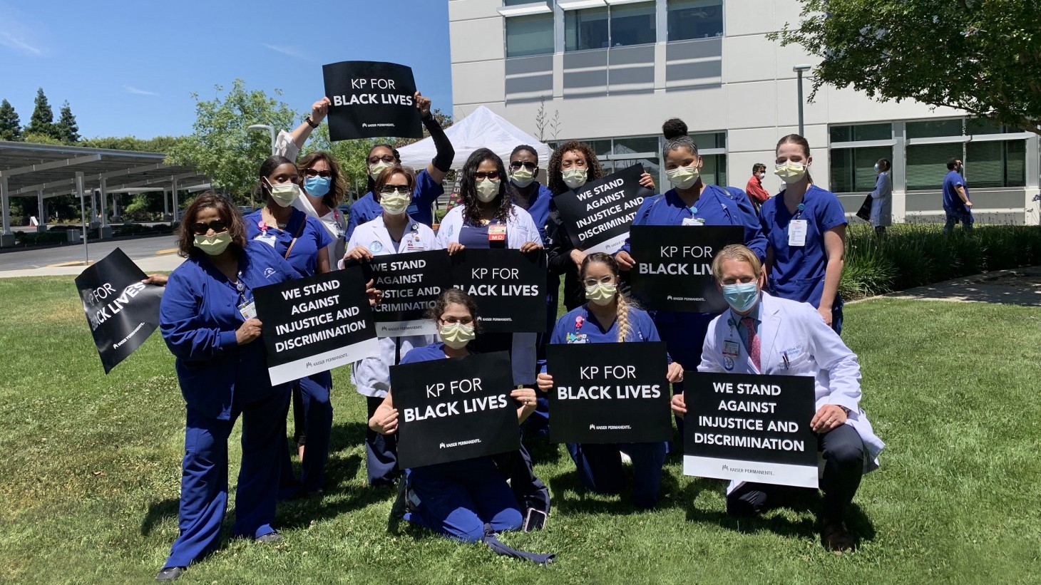 A group of health care workers, wearing scrubs and masks, holding signs that read, 