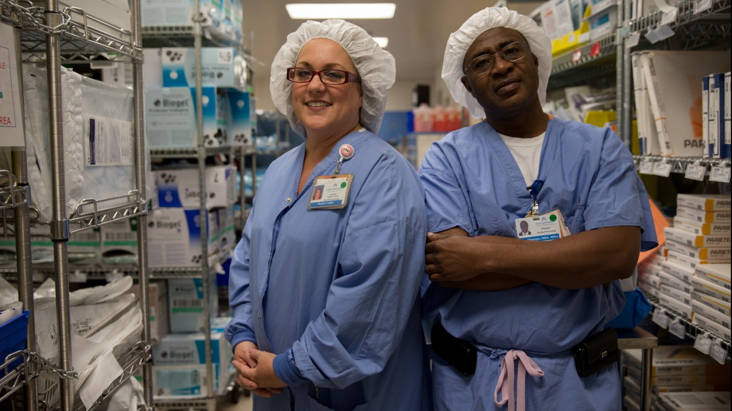 两名医护人员，穿着蓝色的工作服和白色的头巾，在一个储藏室里