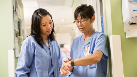两名护士穿着蓝色的磨砂膏，互相交谈