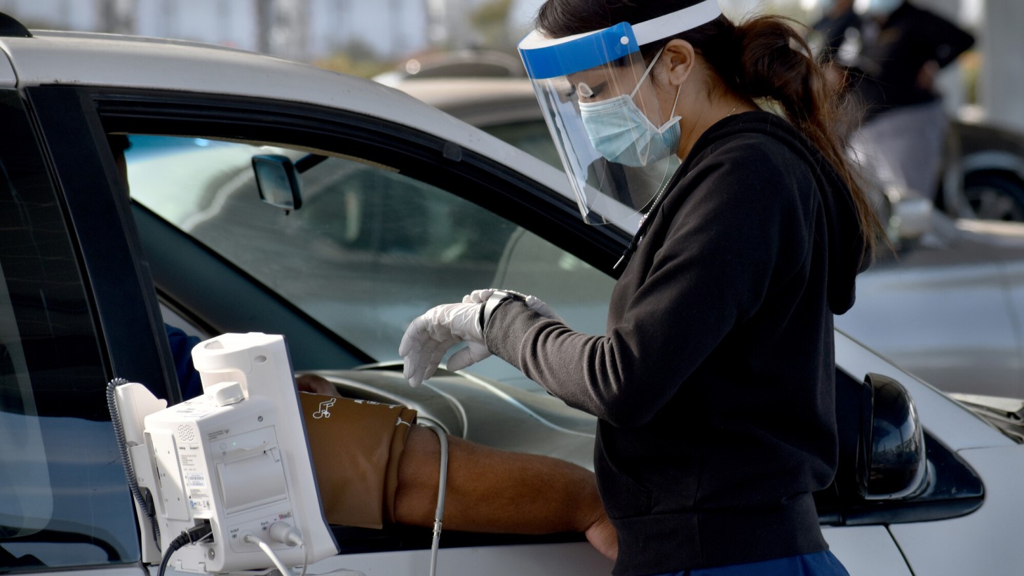 戴着面罩的女人在坐在汽车的乘客座椅上时检查男人的血压