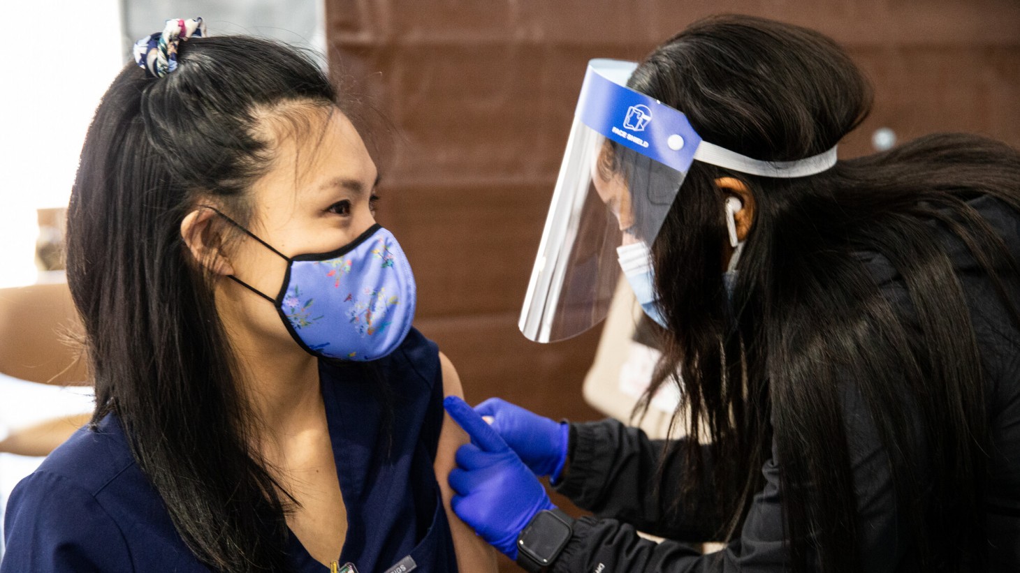 A health care worker wearing a face shield, giving a vaccine to a patient
