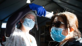 Health care worker wearing face shield takes a patient's temperature
